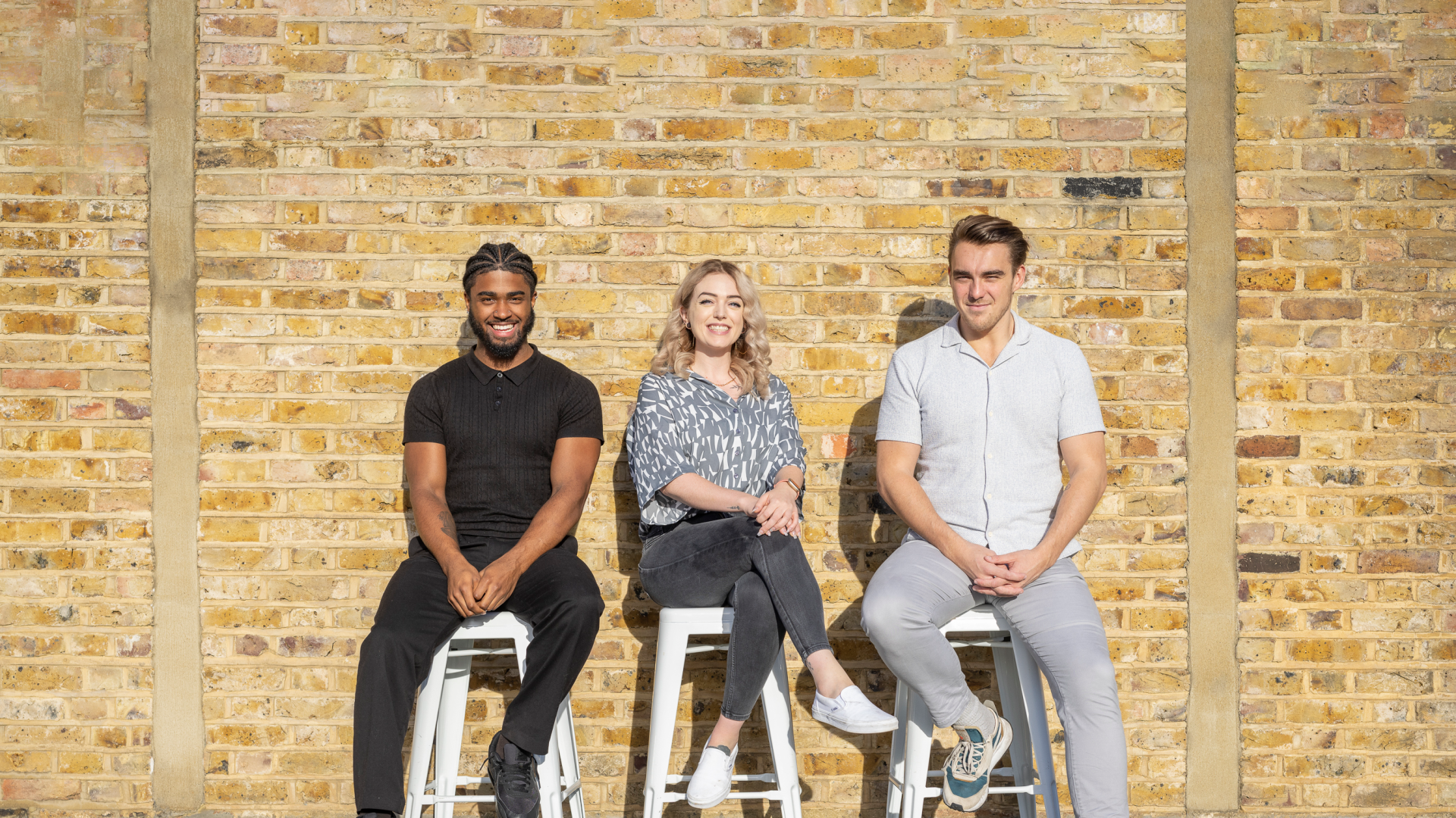 Marketing team sitting on stools against a brick wall and smiling